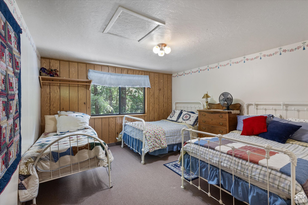 Bedroom with wood walls, a textured ceiling, attic access, and carpet floors