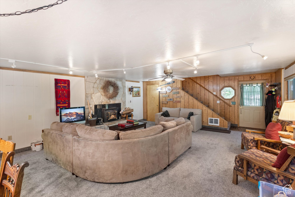 Living area featuring rail lighting, wooden walls, light colored carpet, a ceiling fan, and stairway