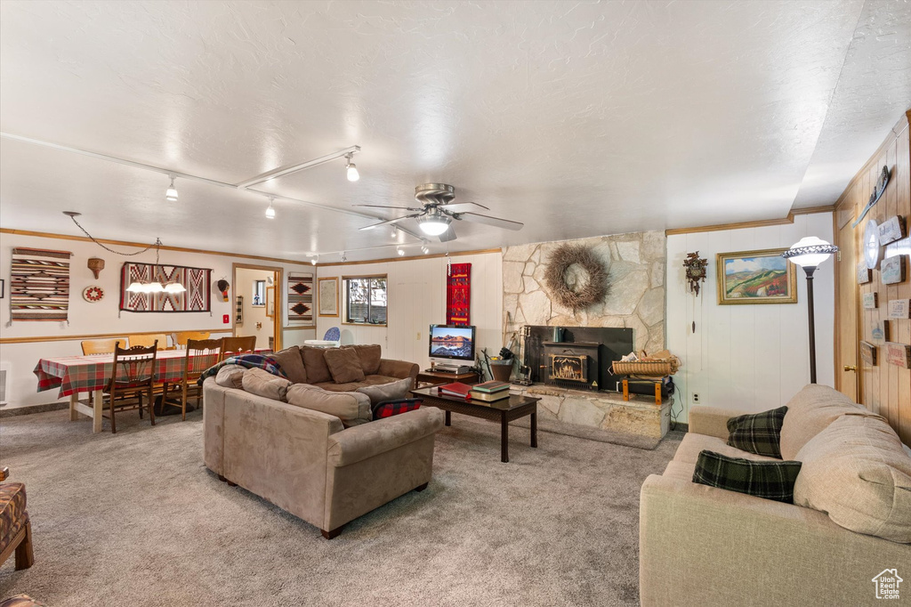 Living room with light colored carpet, a ceiling fan, crown molding, a wood stove, and rail lighting