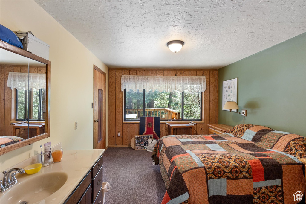 Carpeted bedroom featuring a textured ceiling and wooden walls