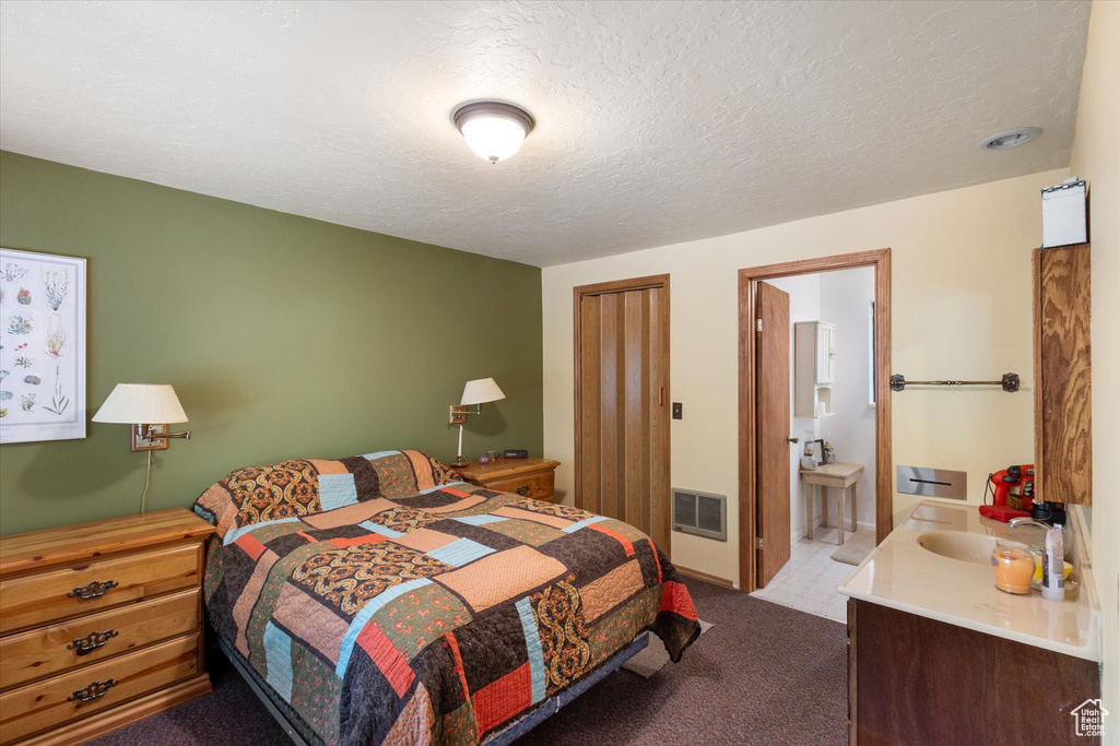 Carpeted bedroom featuring ensuite bath and a textured ceiling