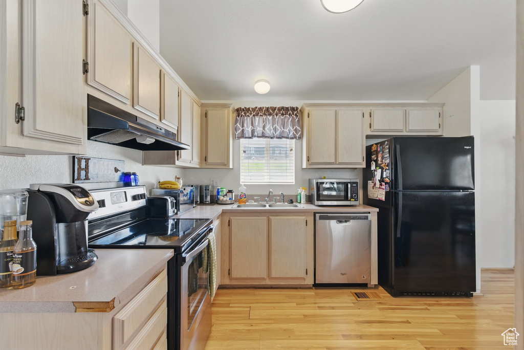 Kitchen with appliances with stainless steel finishes, under cabinet range hood, light countertops, and light brown cabinets