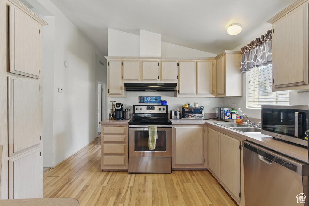 Kitchen featuring stainless steel appliances, lofted ceiling, under cabinet range hood, light wood-type flooring, and light countertops