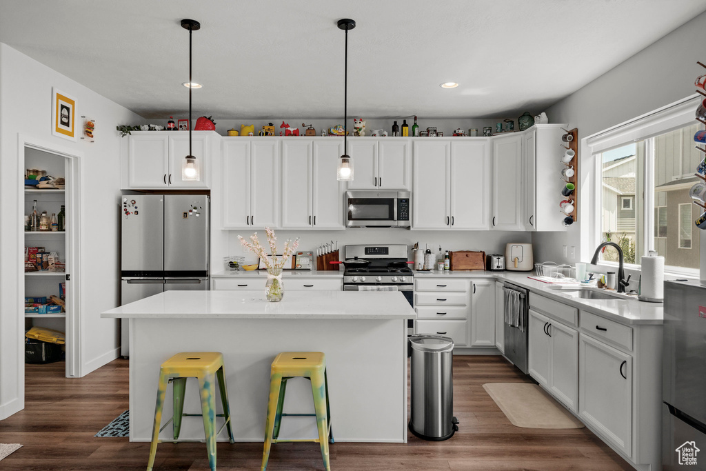 Kitchen with appliances with stainless steel finishes, a kitchen island, dark wood-type flooring, white cabinetry, and recessed lighting