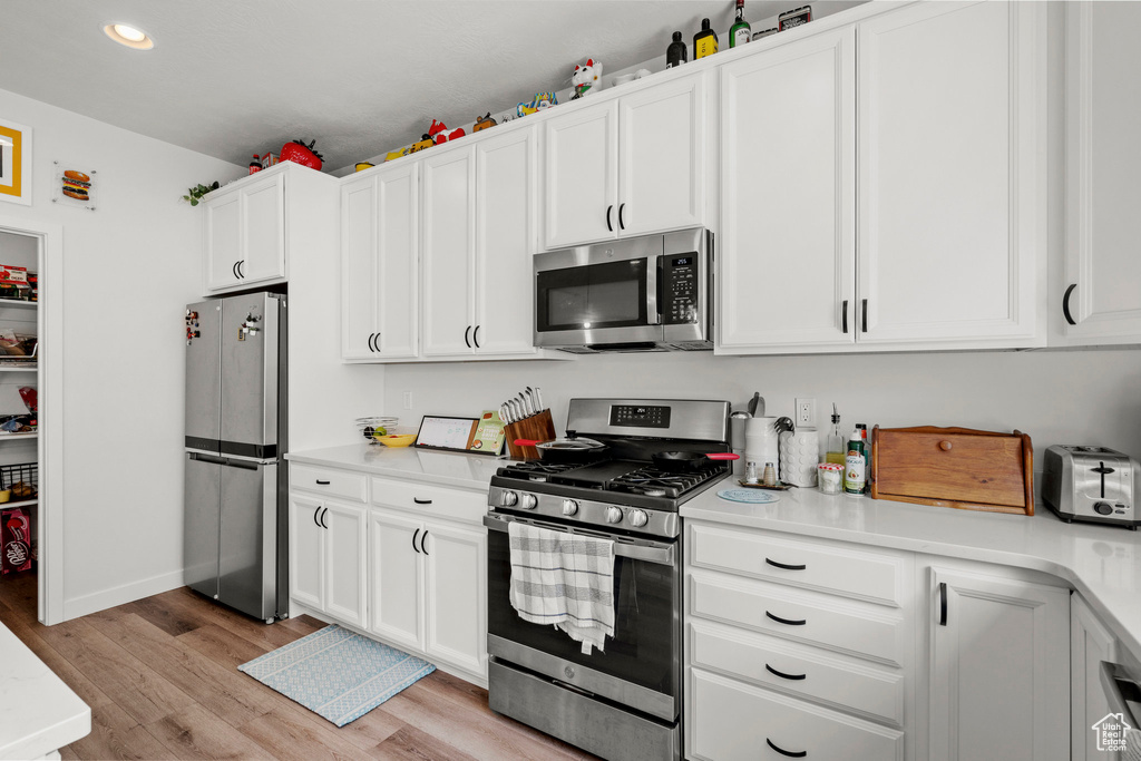 Kitchen featuring appliances with stainless steel finishes, light wood finished floors, light countertops, white cabinetry, and recessed lighting
