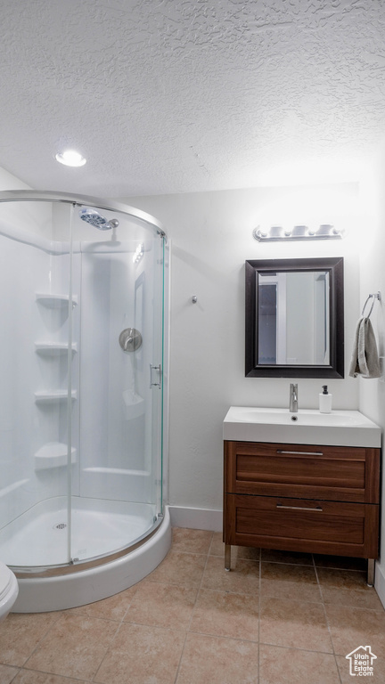 Full bath featuring vanity, a stall shower, a textured ceiling, and tile patterned flooring