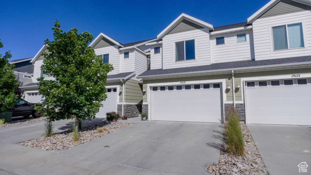 View of property with driveway, stone siding, and an attached garage