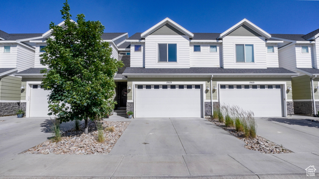 View of property featuring stone siding, a garage, and driveway