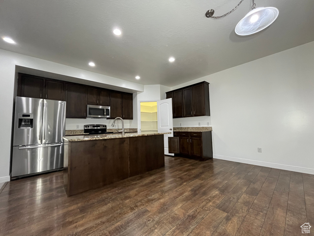 Kitchen with appliances with stainless steel finishes, dark brown cabinets, dark wood-type flooring, a kitchen island with sink, and recessed lighting