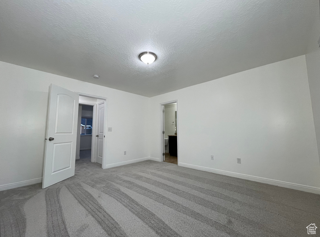 Unfurnished bedroom featuring carpet, a textured ceiling, and a walk in closet