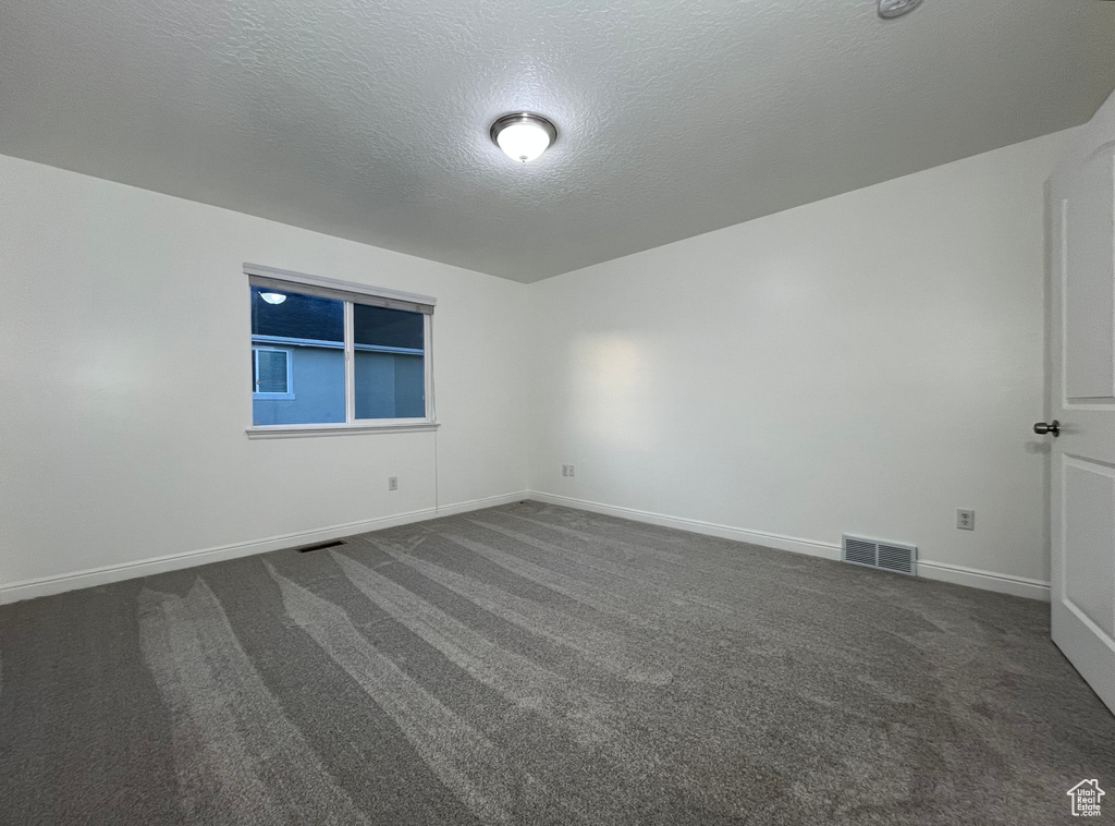 Spare room featuring dark colored carpet and a textured ceiling
