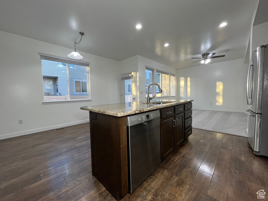 Kitchen featuring stainless steel appliances, dark wood finished floors, dark brown cabinetry, light stone counters, and a ceiling fan