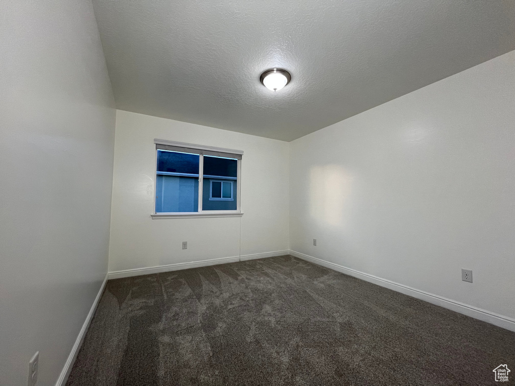 Empty room with dark carpet and a textured ceiling