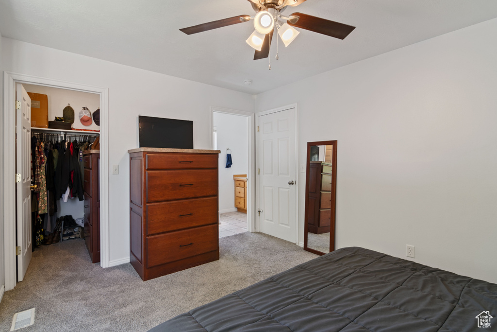 Bedroom featuring light colored carpet, a closet, a walk in closet, and a ceiling fan