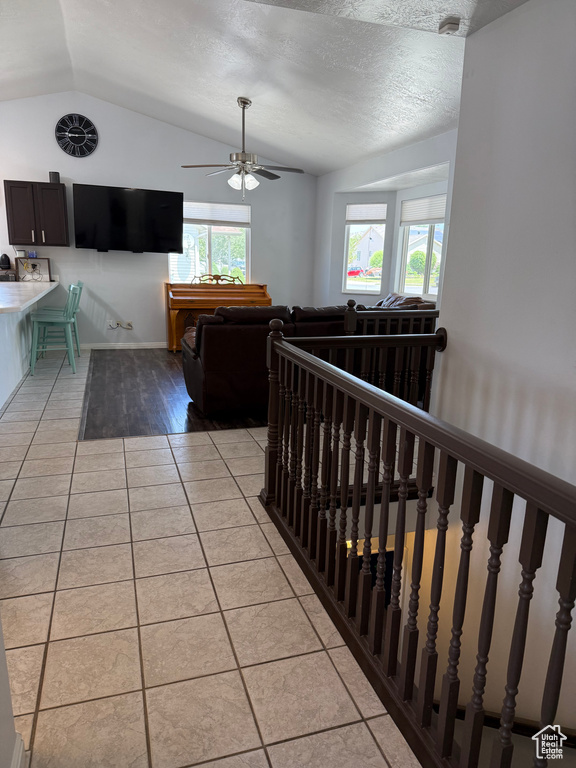 Hallway featuring vaulted ceiling, light tile patterned flooring, an upstairs landing, and a textured ceiling