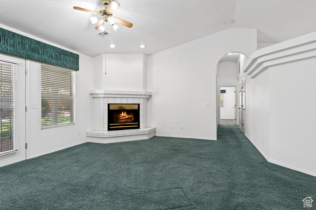 Unfurnished living room featuring ceiling fan, dark carpet, a tiled fireplace, arched walkways, and baseboards