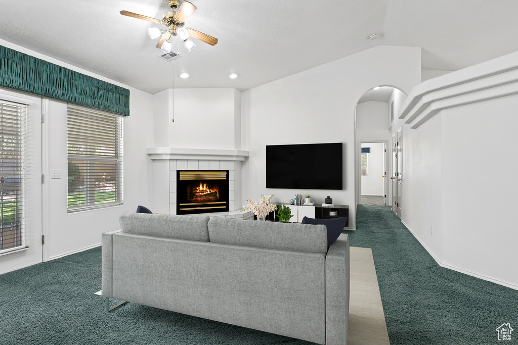 Living room featuring carpet, ceiling fan, a tile fireplace, arched walkways, and recessed lighting