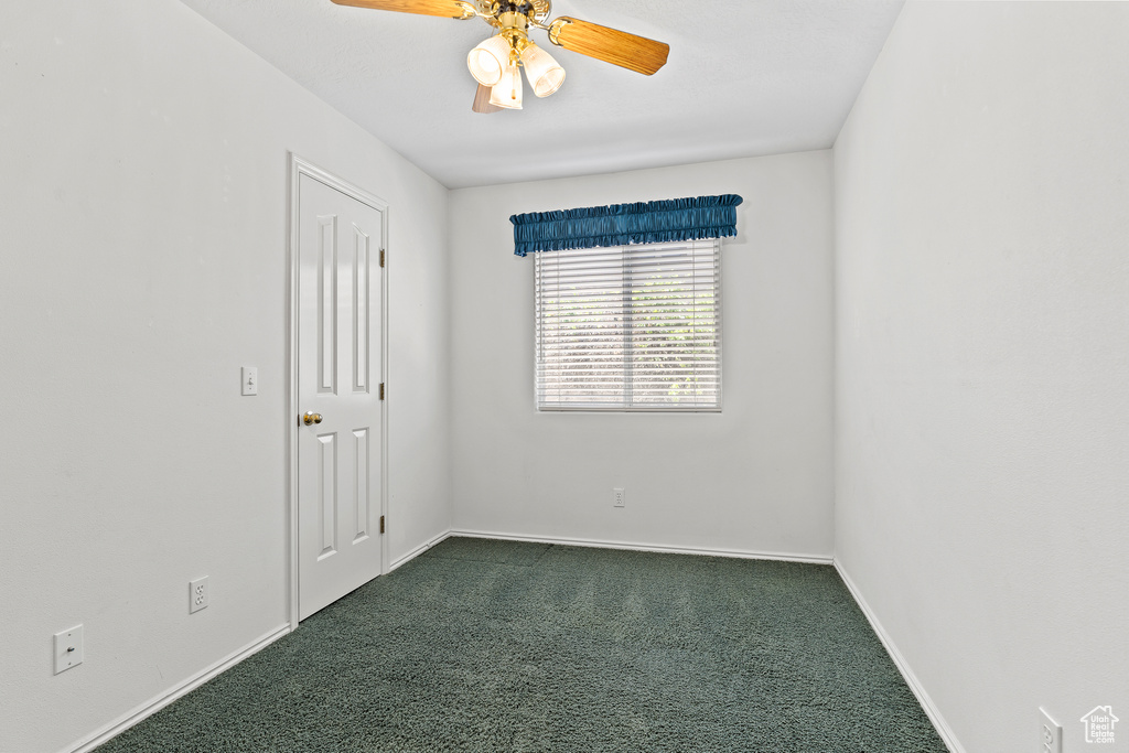 Empty room with dark carpet, baseboards, and ceiling fan