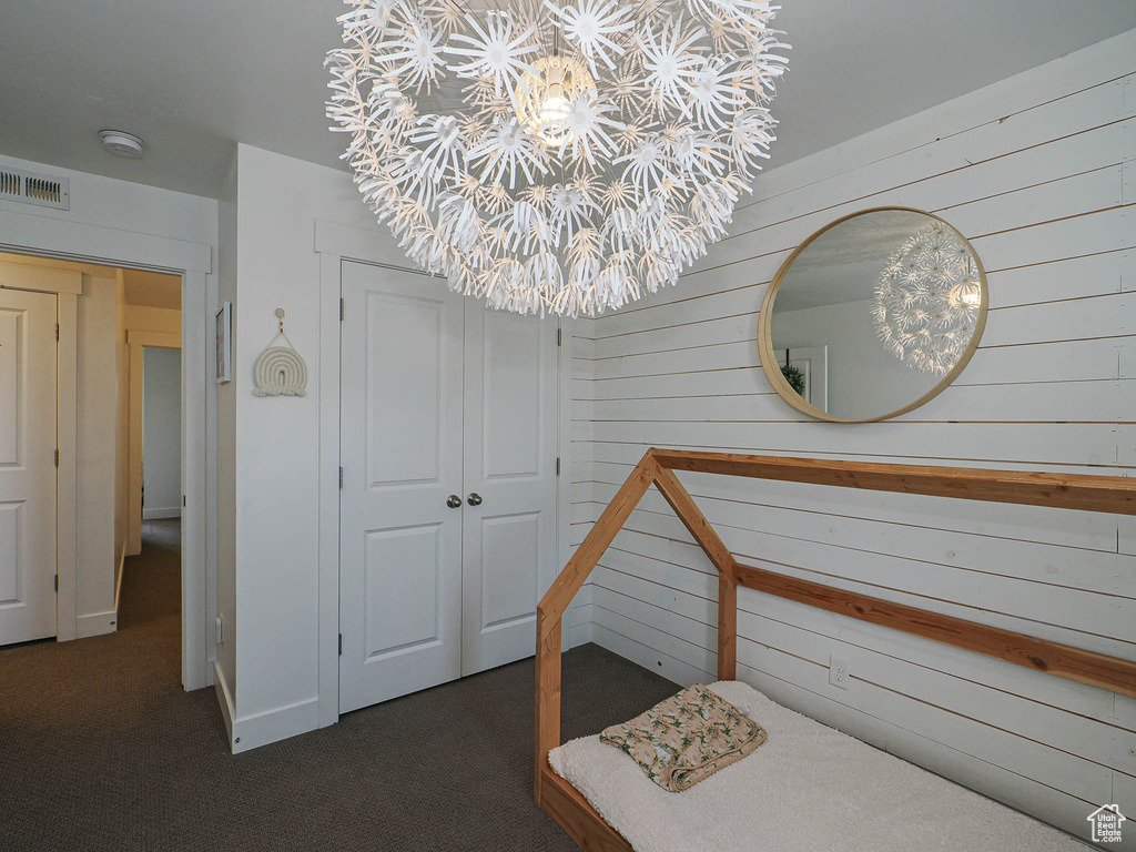 Bedroom featuring wood walls, a closet, a chandelier, and dark colored carpet