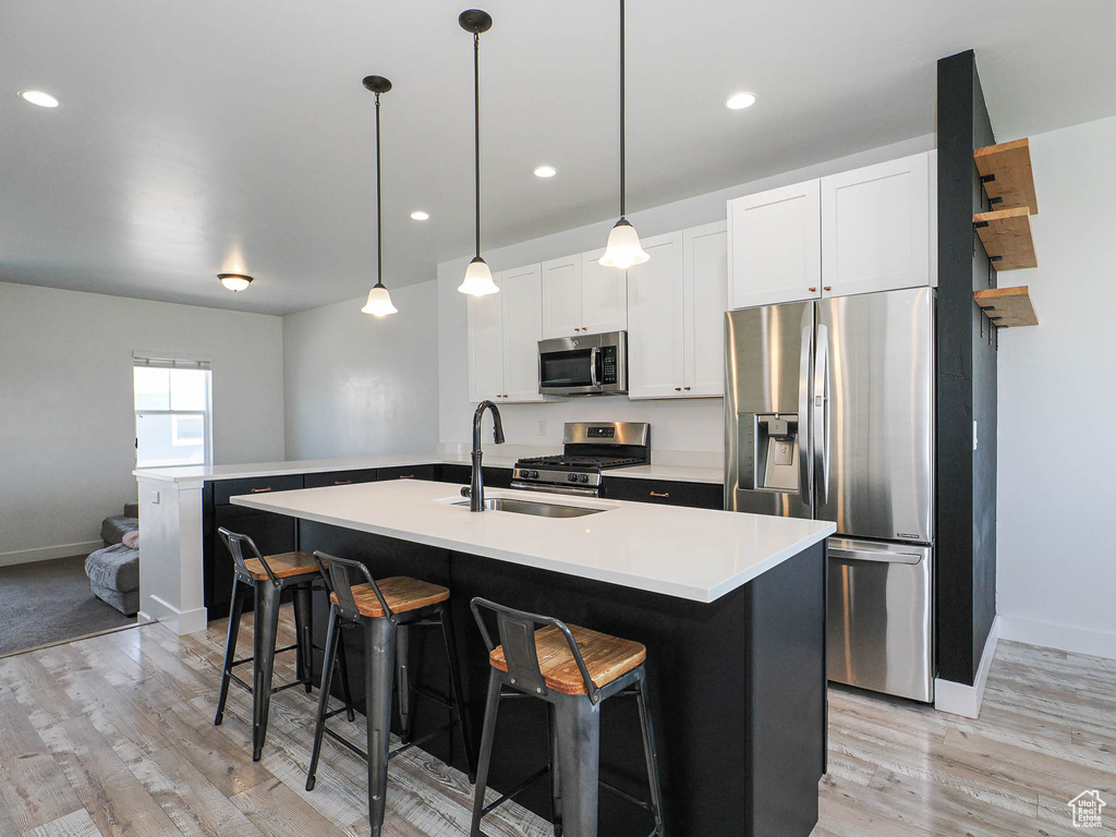 Kitchen featuring appliances with stainless steel finishes, light wood-type flooring, a kitchen bar, light countertops, and a center island with sink