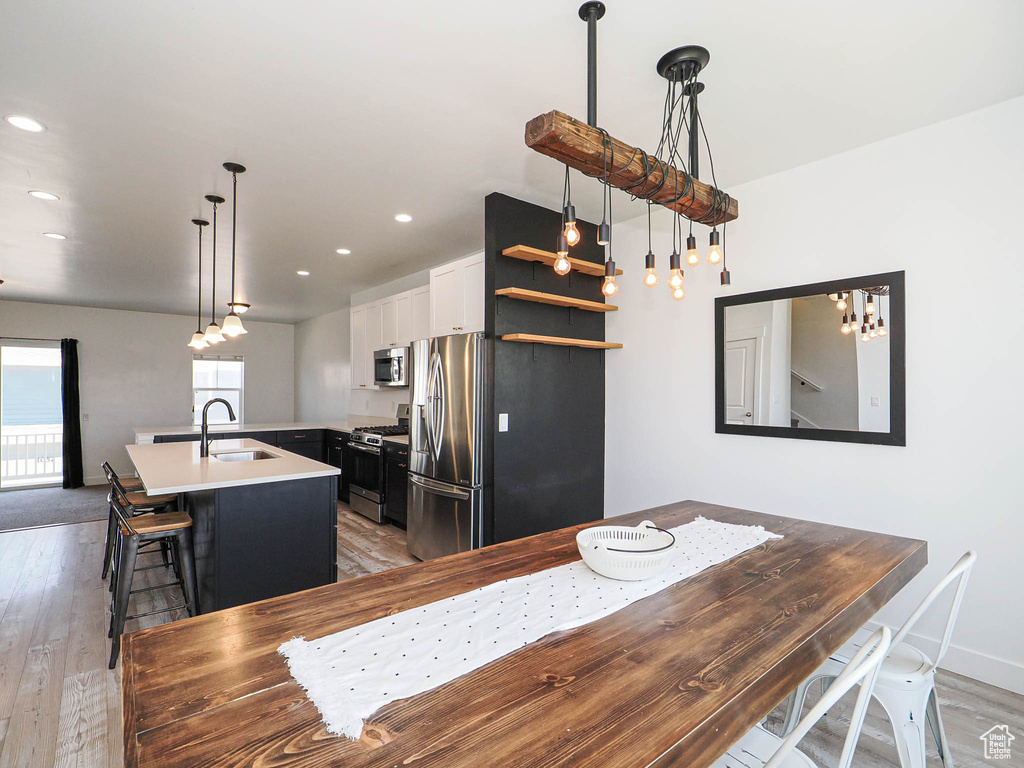 Kitchen with stainless steel appliances, light wood-style floors, a center island with sink, light countertops, and recessed lighting