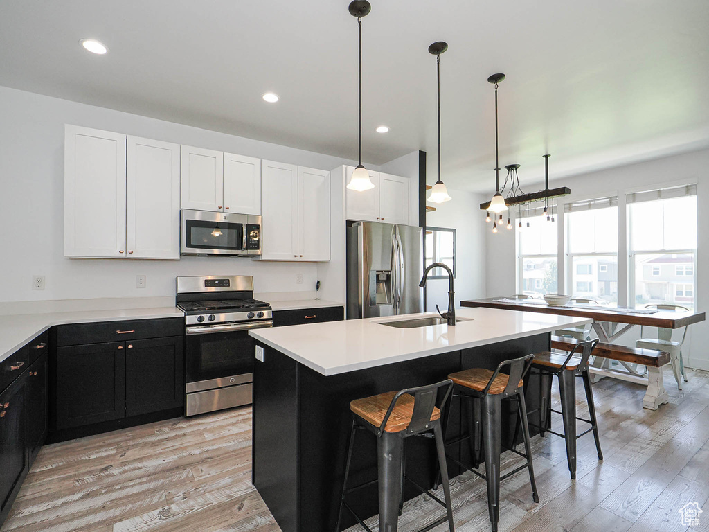 Kitchen featuring appliances with stainless steel finishes, a kitchen bar, light wood finished floors, a center island with sink, and recessed lighting
