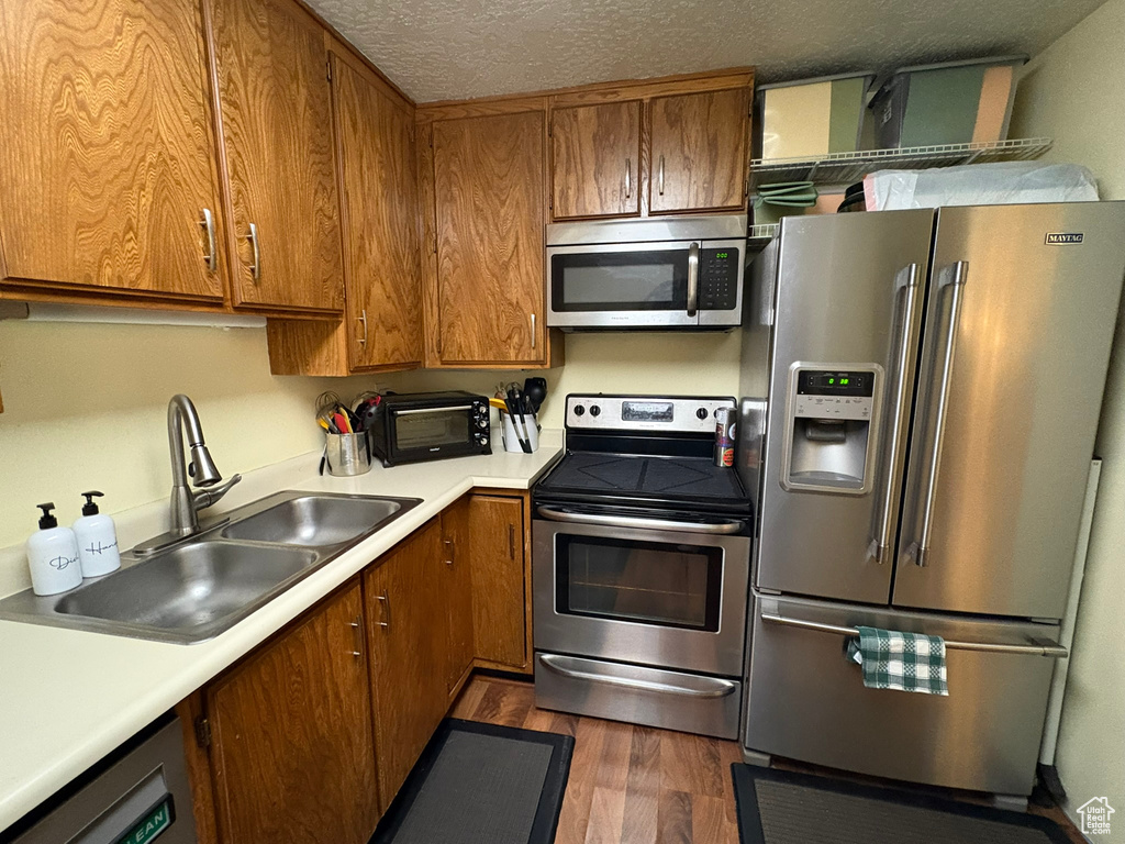 Kitchen featuring stainless steel appliances, brown cabinets, dark wood finished floors, and a textured ceiling
