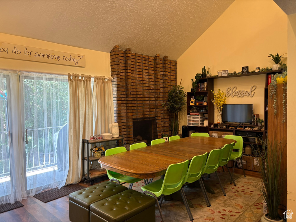 Dining space featuring lofted ceiling, a brick fireplace, wood finished floors, and a textured ceiling