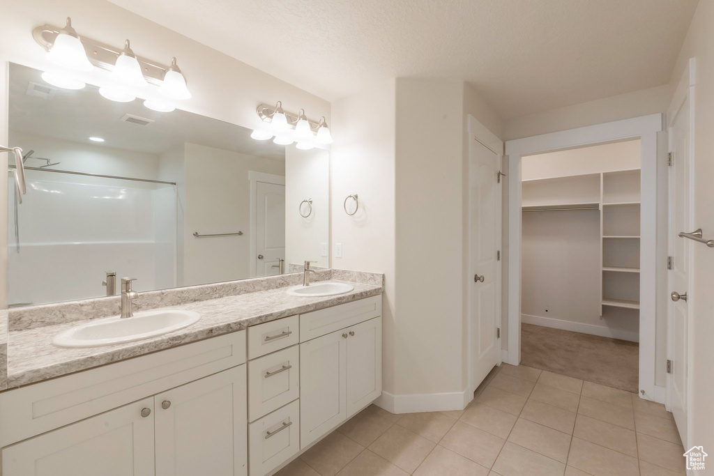 Full bathroom with double vanity, tile patterned flooring, a shower, a spacious closet, and baseboards