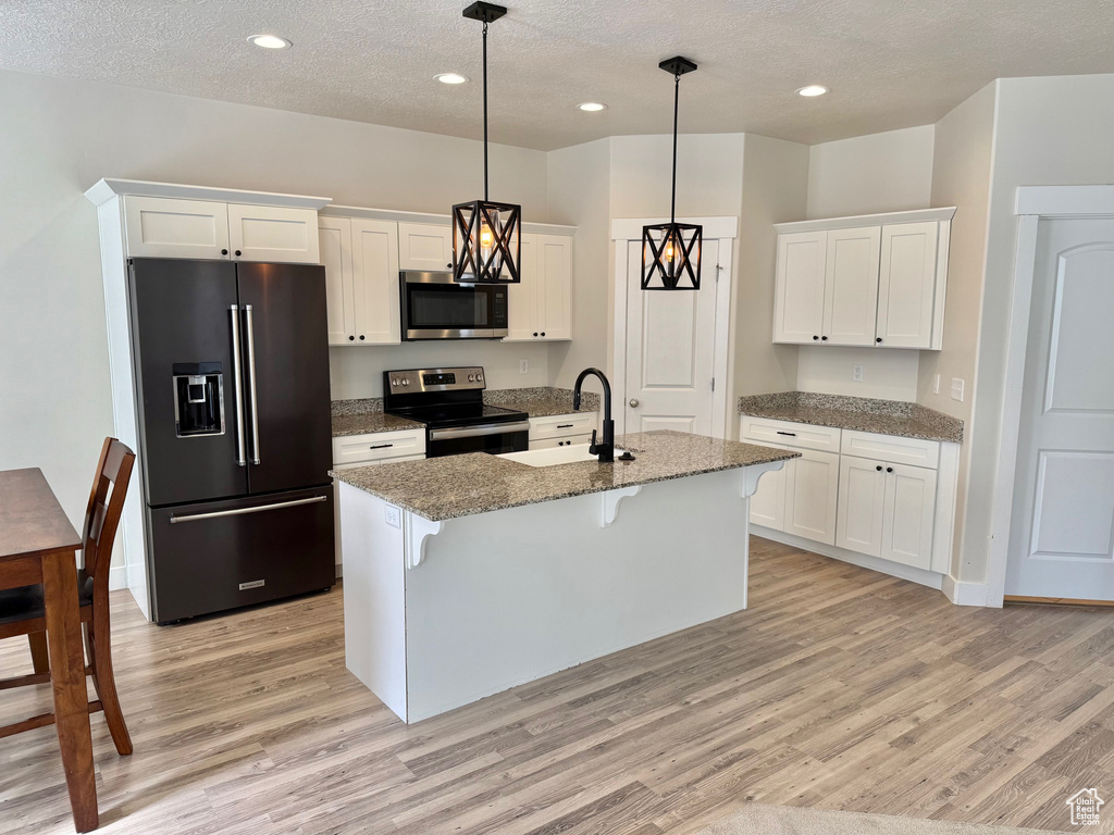 Kitchen featuring high end refrigerator, electric stove, stainless steel microwave, light wood-style floors, and a kitchen breakfast bar