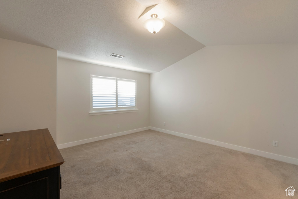 Spare room with vaulted ceiling, light colored carpet, and baseboards