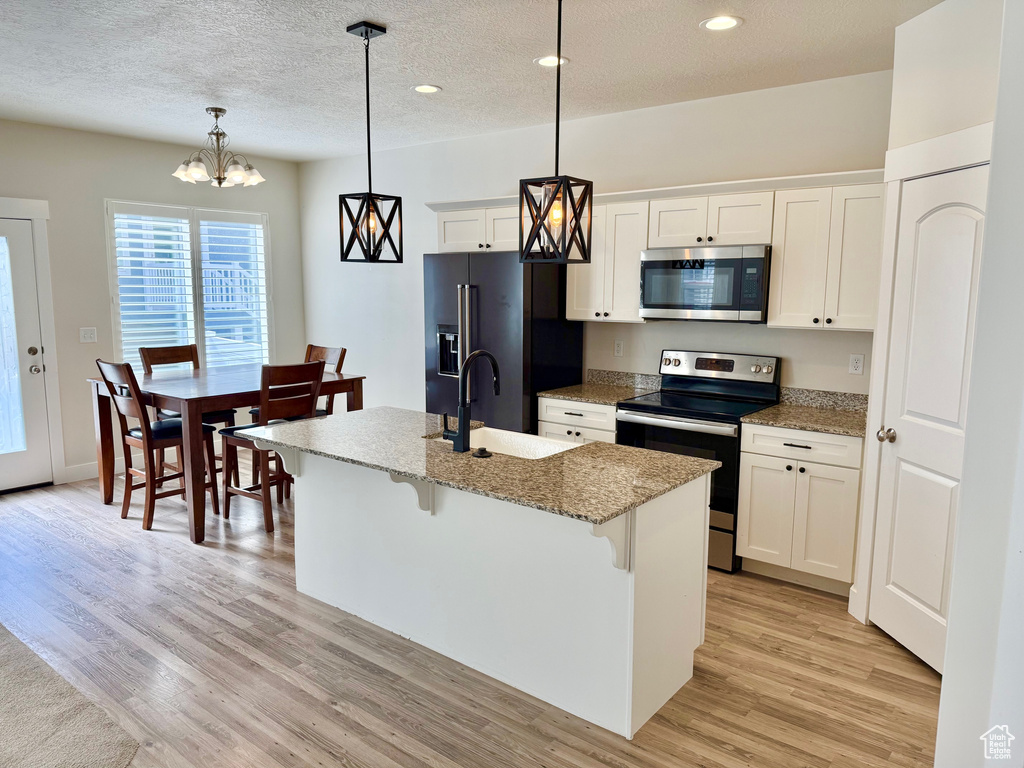 Kitchen featuring stainless steel appliances, light wood-style floors, a kitchen breakfast bar, a center island with sink, and recessed lighting