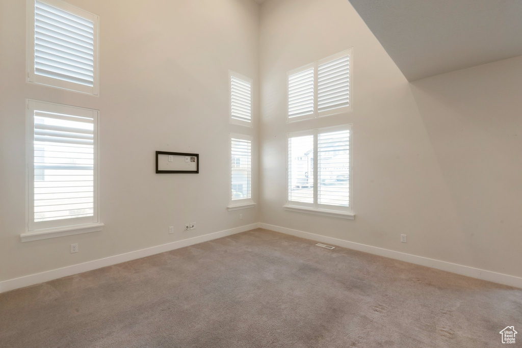 Empty room featuring a towering ceiling, light colored carpet, and baseboards