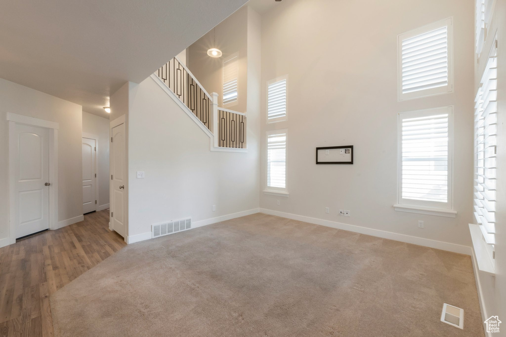 Unfurnished living room with baseboards, a towering ceiling, plenty of natural light, carpet, and stairway