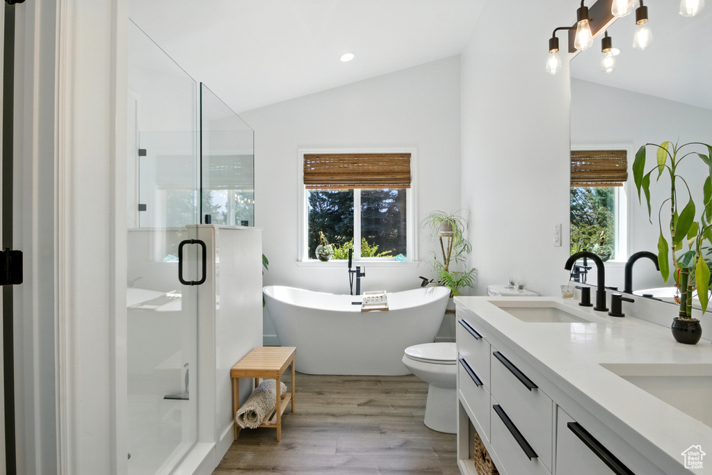 Bathroom featuring lofted ceiling, double vanity, wood finished floors, a stall shower, and a freestanding tub