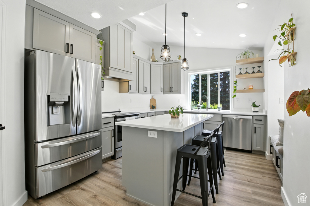 Kitchen featuring stainless steel appliances, open shelves, lofted ceiling, light countertops, and a center island