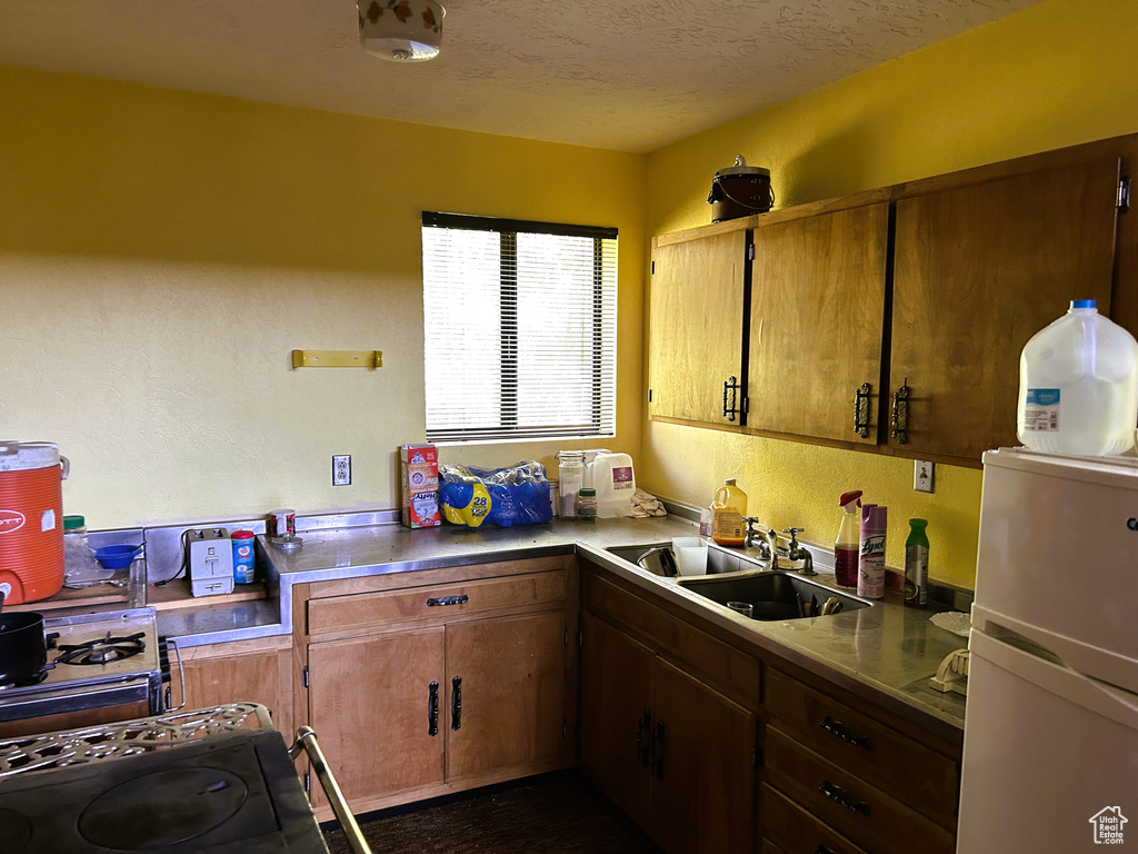 Kitchen with refrigerator, stove, a textured ceiling, and brown cabinetry