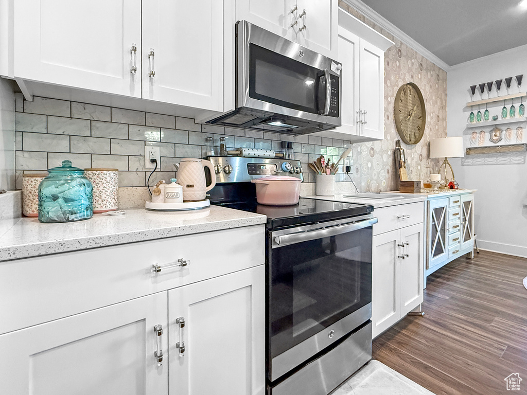 Kitchen featuring appliances with stainless steel finishes, ornamental molding, decorative backsplash, white cabinetry, and light stone countertops