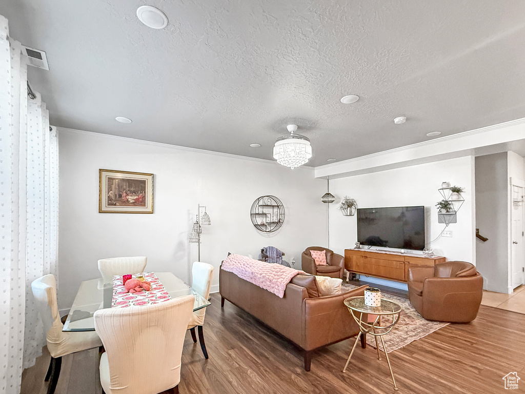 Living room with wood finished floors, a textured ceiling, ornamental molding, and a chandelier