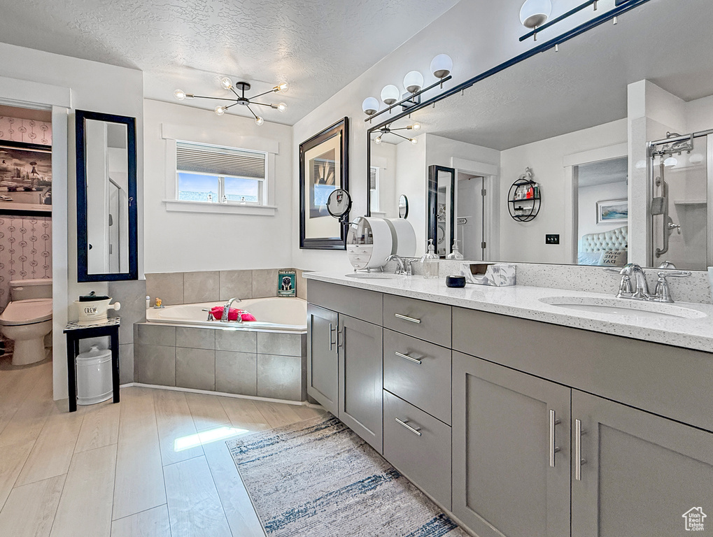 Bathroom featuring double vanity, a garden tub, wood finished floors, a chandelier, and a textured ceiling
