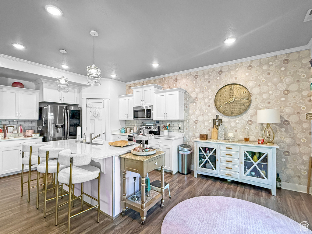 Kitchen with appliances with stainless steel finishes, crown molding, a breakfast bar area, backsplash, and white cabinets