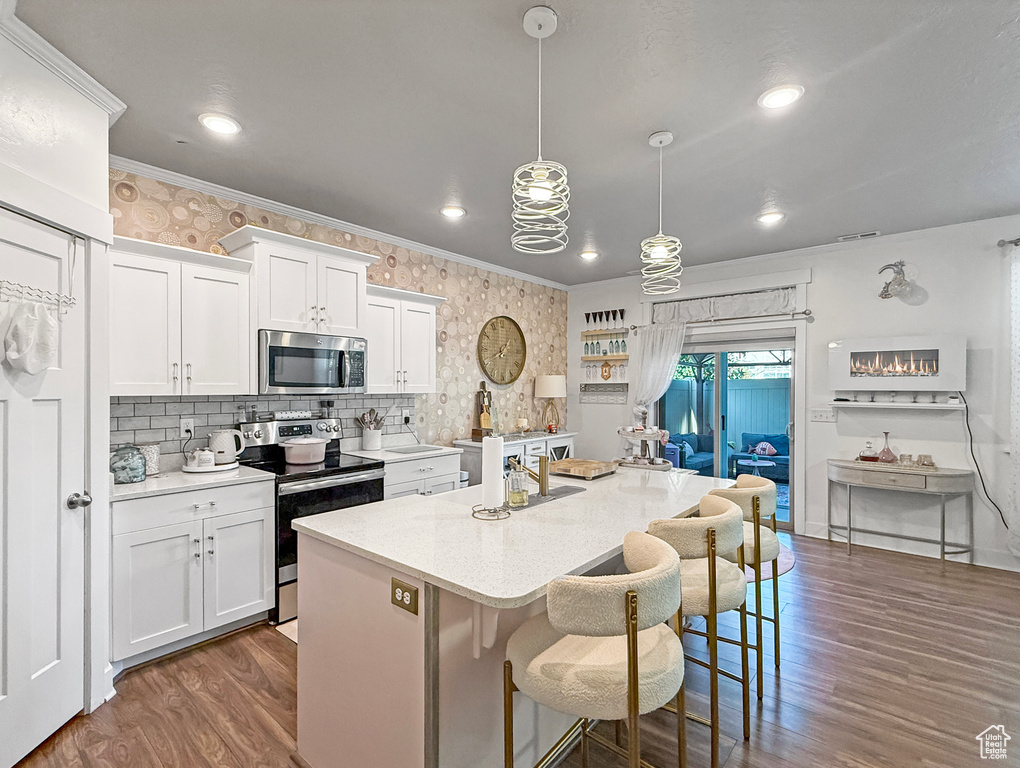 Kitchen with appliances with stainless steel finishes, dark wood-style floors, light countertops, white cabinets, and crown molding