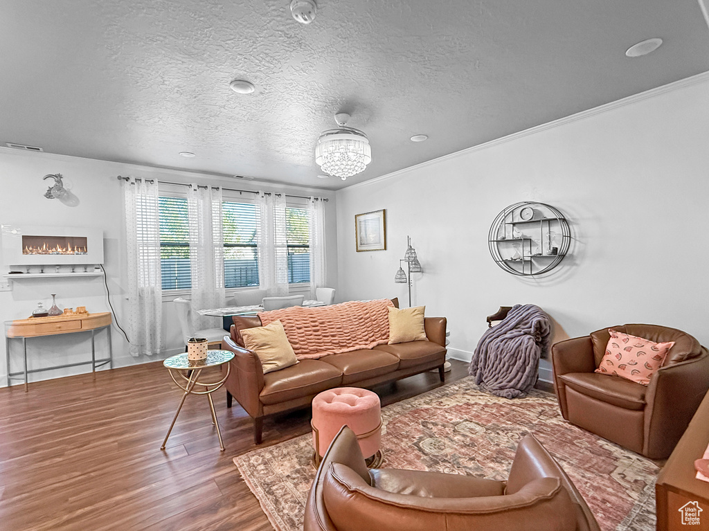 Living area featuring wood finished floors, a textured ceiling, crown molding, and a chandelier