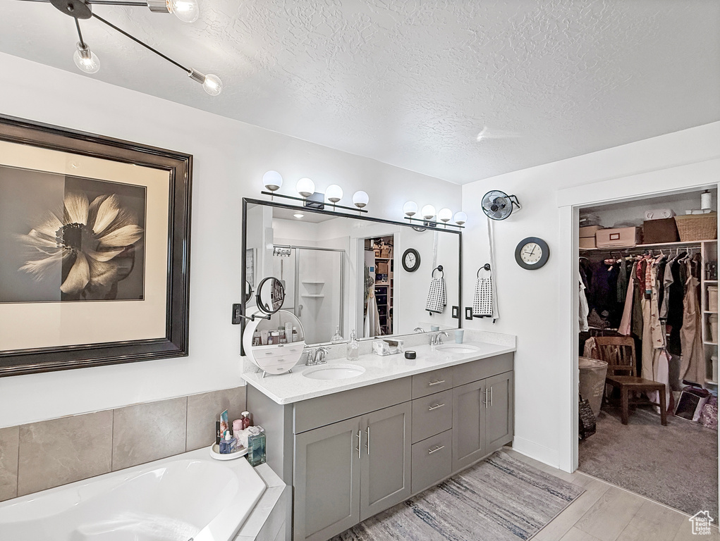 Bathroom with a walk in closet, a textured ceiling, double vanity, a garden tub, and wood finished floors