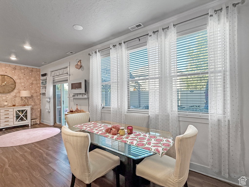 Dining space with wood finished floors, crown molding, and wallpapered walls