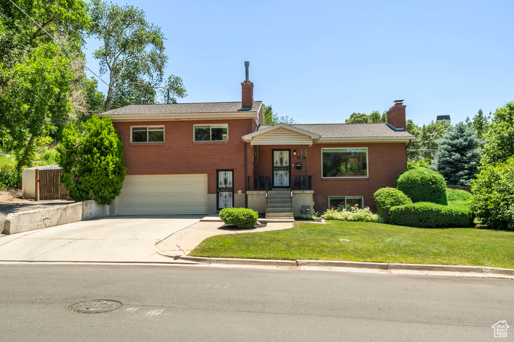 Tri-level home featuring a garage, concrete driveway, a chimney, and brick siding