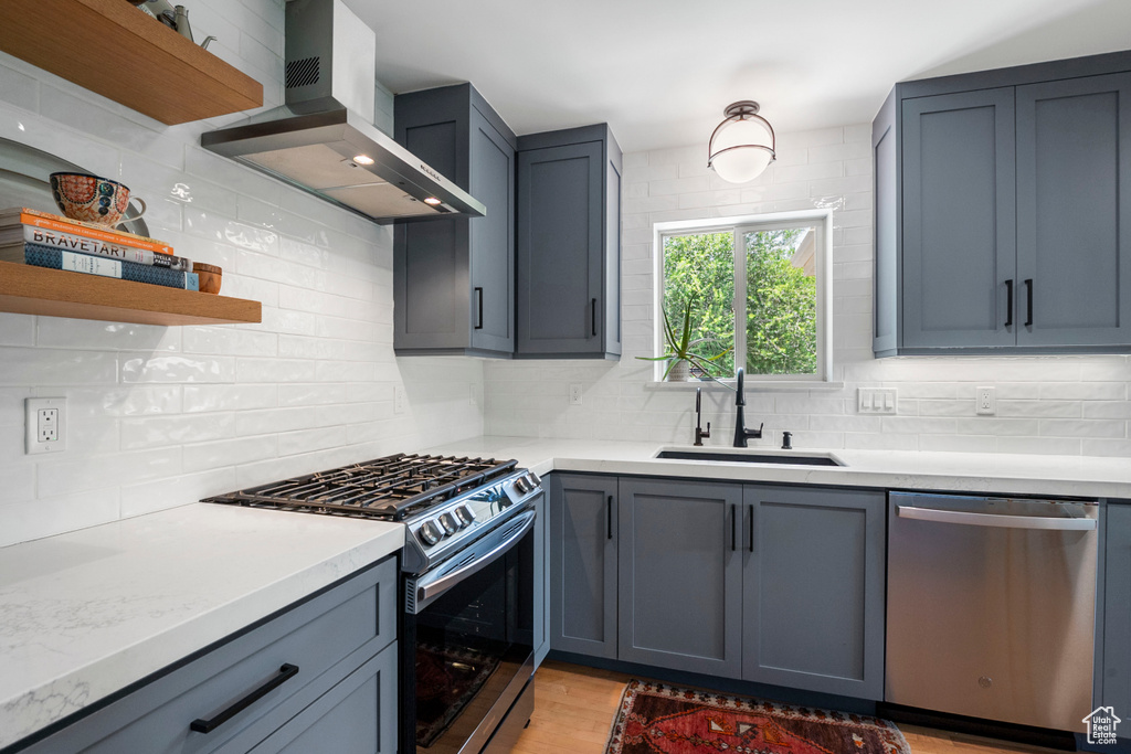 Kitchen with stainless steel appliances, wall chimney range hood, open shelves, and tasteful backsplash