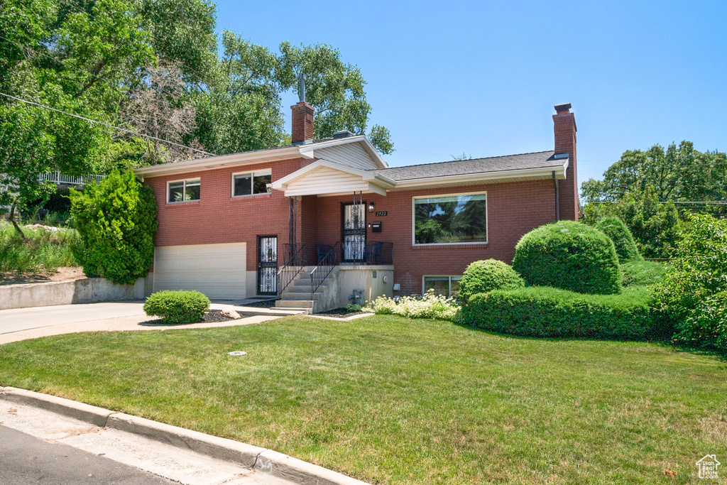 Tri-level home featuring a chimney, brick siding, and driveway