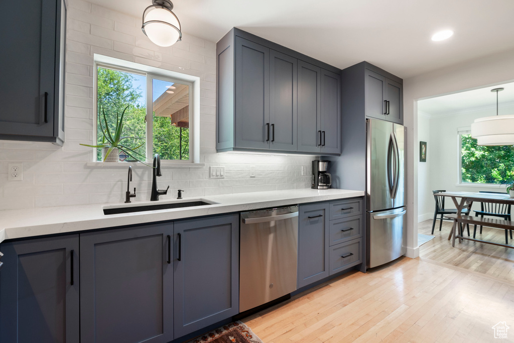 Kitchen with stainless steel appliances, light wood finished floors, tasteful backsplash, decorative light fixtures, and light stone counters