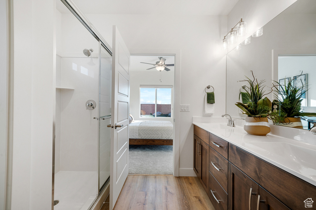 Bathroom featuring wood finished floors, double vanity, a stall shower, ensuite bath, and a ceiling fan